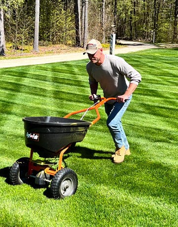 man pushing a fertilizer spreader over green lawn