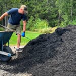 man with pitchfork loading black mulch into wheelbarrow